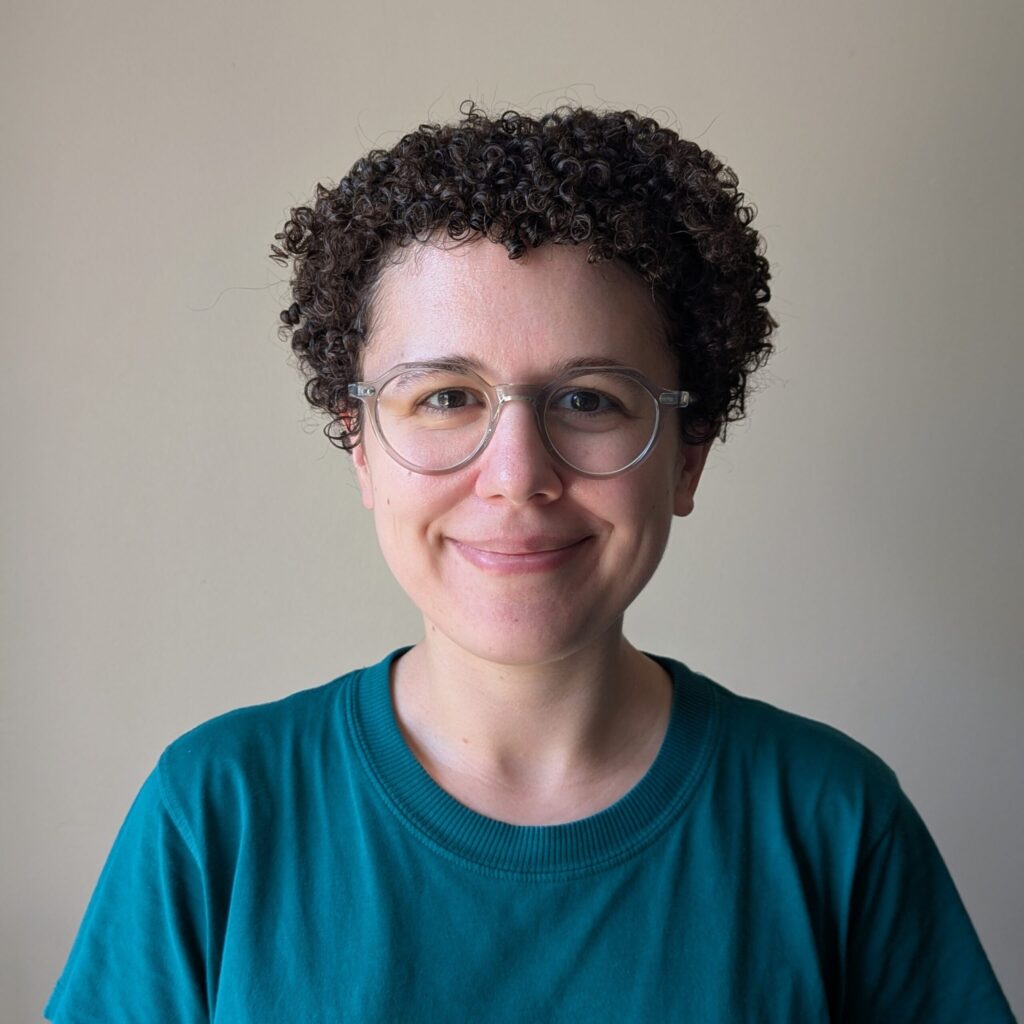 A smiling, non-binary woman with glasses and short, curly hair.