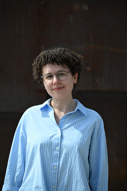 A smiling, non-binary woman with glasses and short, curly hair.