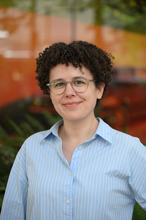 A smiling, non-binary woman with glasses and short, curly hair.
